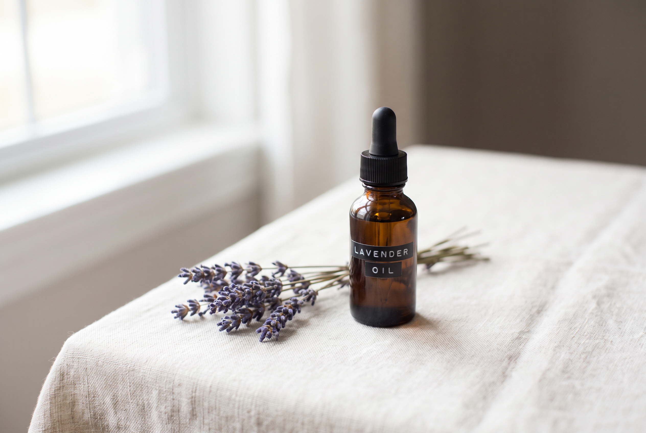 An amber bottle labelled Lavender Oil with a sprig of fresh lavender on linen